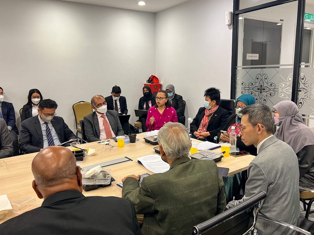 Individuals sitting around a table while Nadiah from KAMY is speaking. She is wearing a pink kebaya/baju kurung.