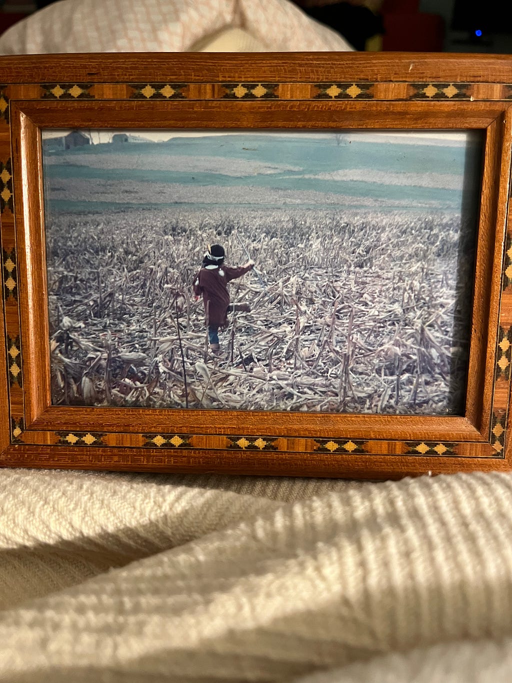 A little boy running into a field of recent harvested crop in a Indian outfit. The image shows him doing a side-kick.