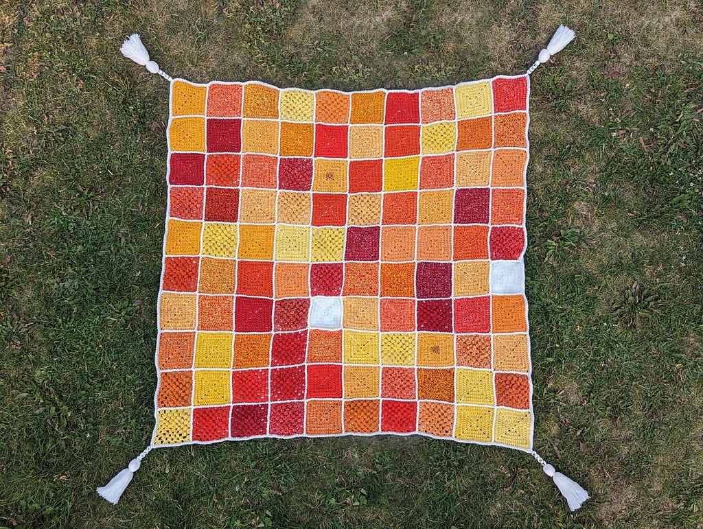 The blanket is laid out on the grass with the four tassels extending out from each corner.