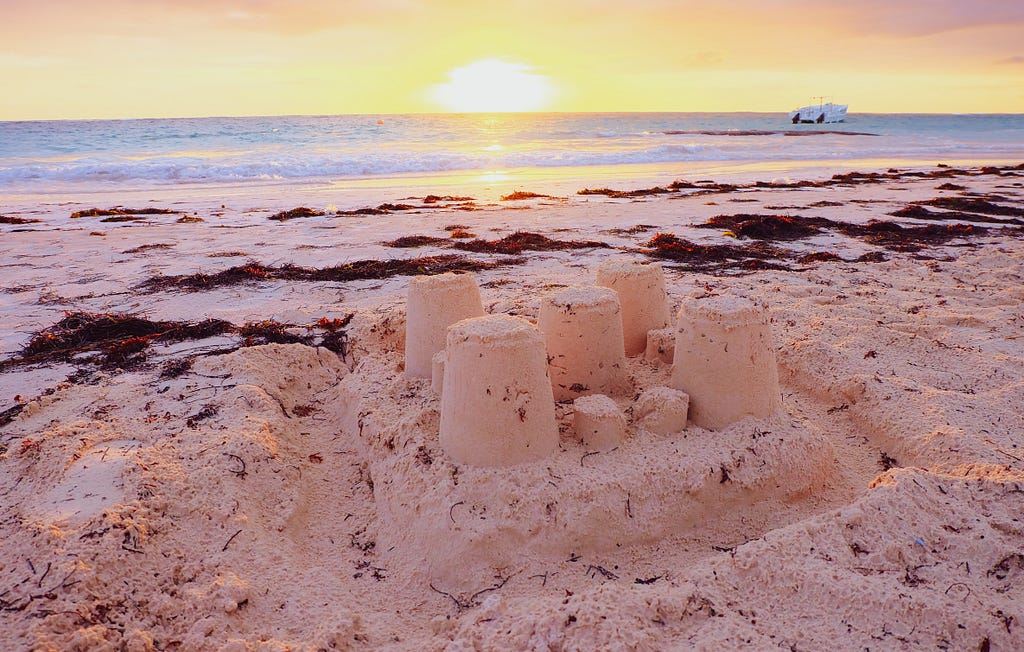 A sandcastle on a beach with the sun setting in the background.