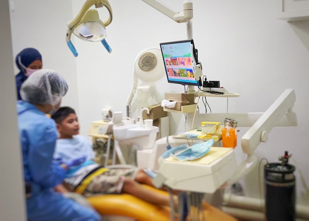 A child, dentist, and nurse. The child is seating on a dental chair.
