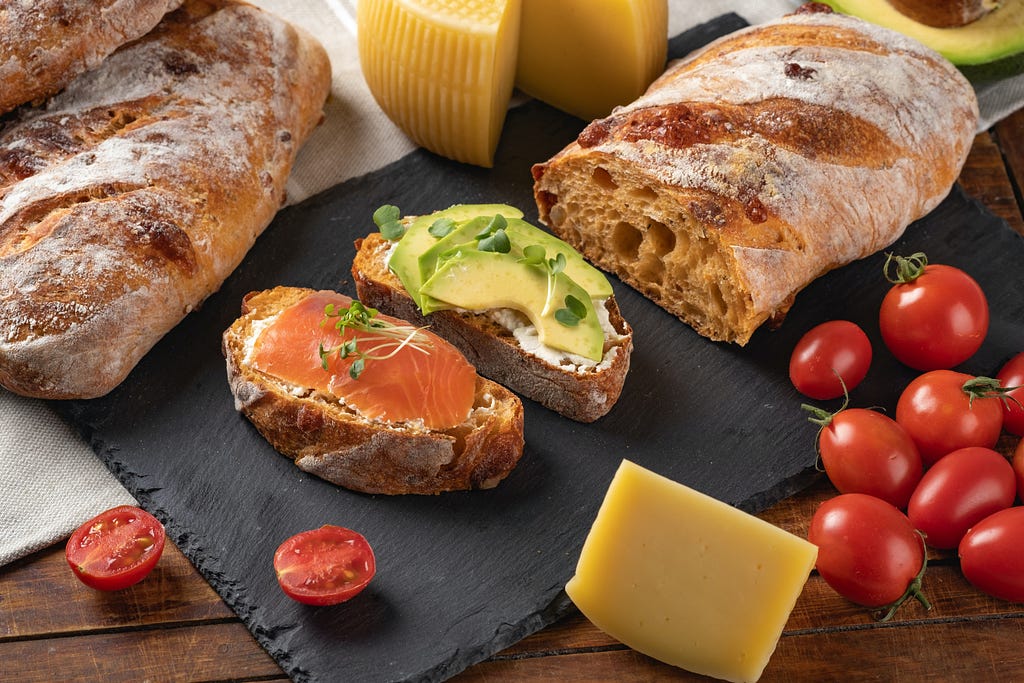 foto de um pão com fatias cortadas acompanhadas de queijo, presunto cru e tomates