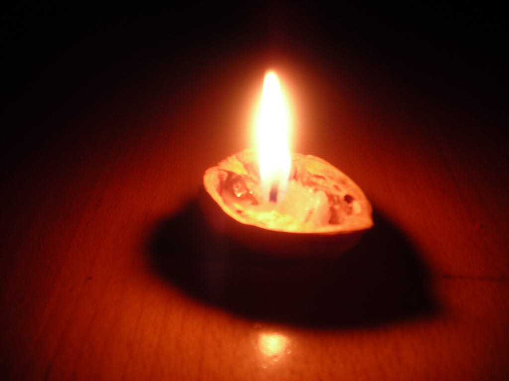 A small candle boat made from a walnut shell, lit against a dark background