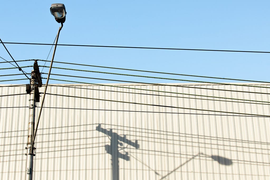 A camera attached to a utility pole with wires against a beige building and blue sky.