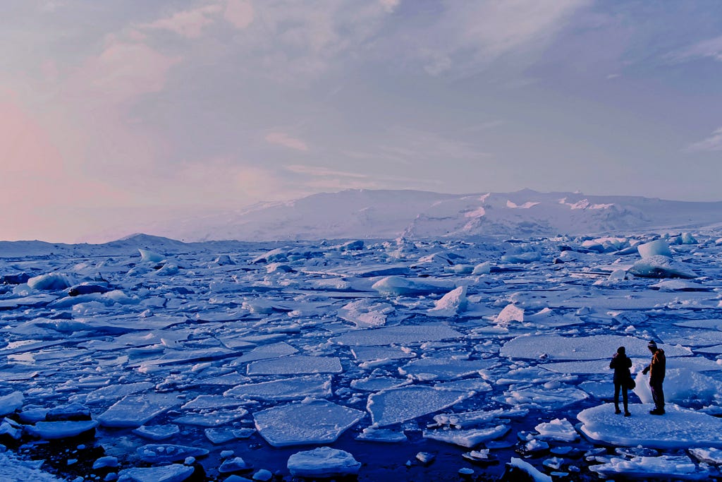 Two people standing on melting glacial ice in the sea