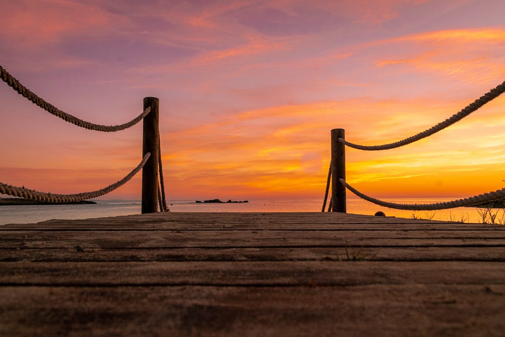 A boardwalk looking over the sea with a sunset behind it