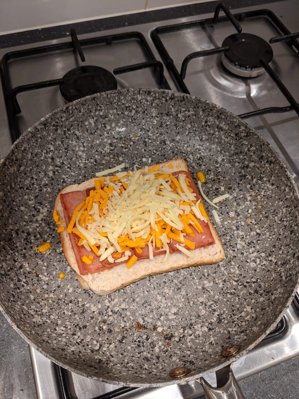 A spam and cheese toastie being cooked in a pan on a hob.