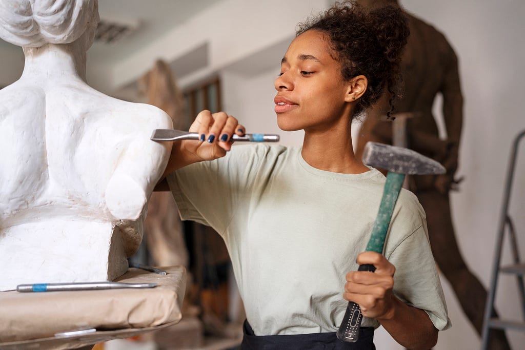 A picture of a Lady sculpting with a Hammer and Chisel.