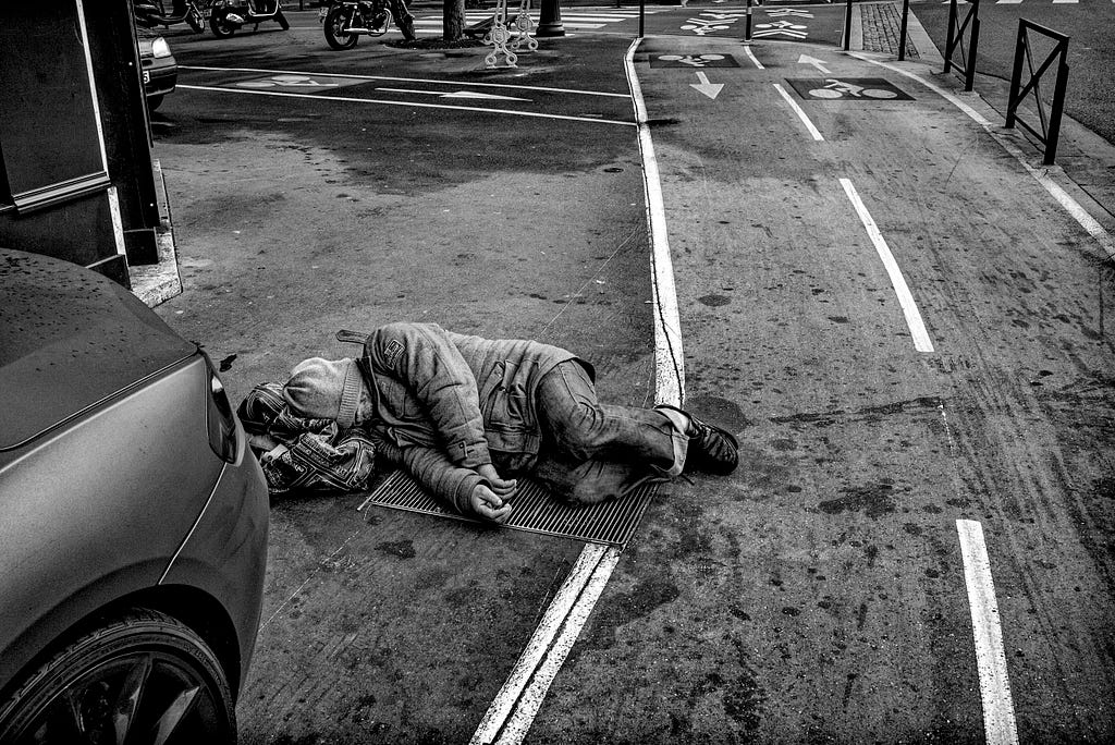 The Paris Olympics are due to start on the 24th of July. While the number of unhoused varies wildly, the city is attempting to move them out before the games start. Unhoused man sleeps on the street across from the Seine. Paris, France. Photo: Robert Gumpert 12 January 2016
