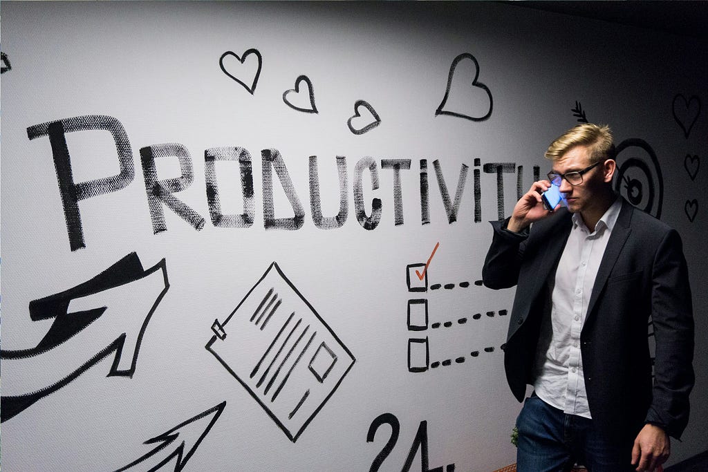 A young man talking on his phone in front of a wall with a big writing “productivity”