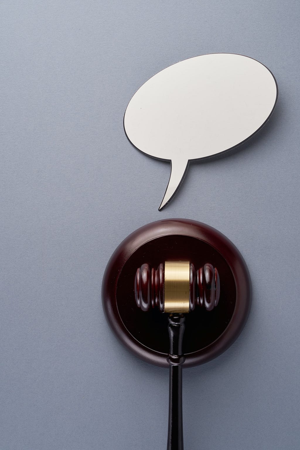 A wooden gavel rests upon its striking plate. A speech bubble sits above the gavel & plate, as if the wooden pieces have something to say. The speech bubble is empty.