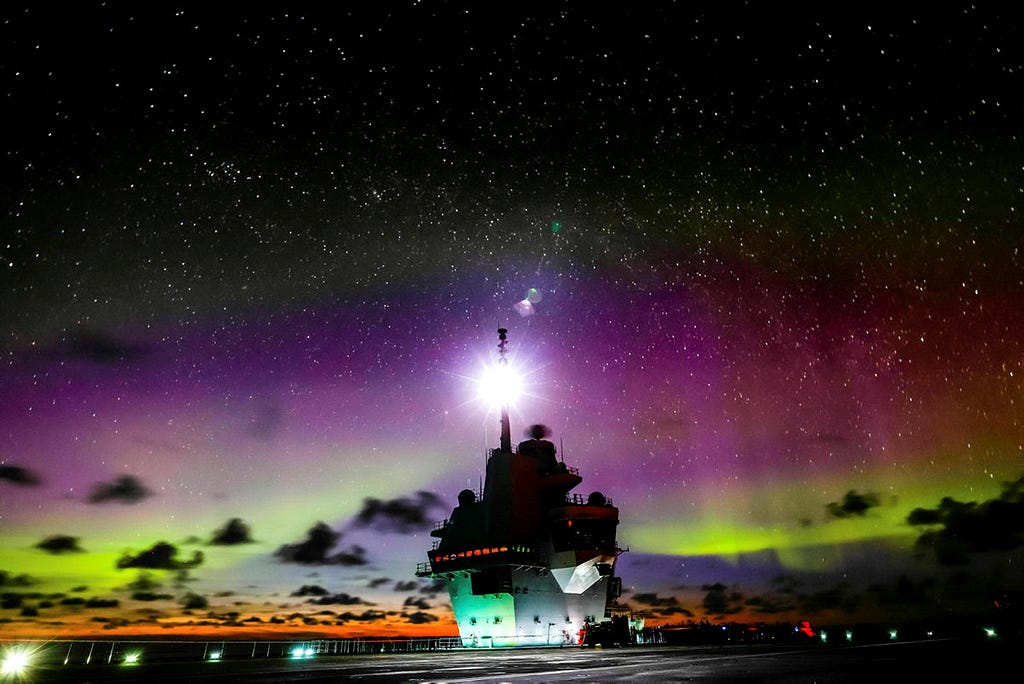 Royal Navy Aircraft Carrier sails under the Northern Lights