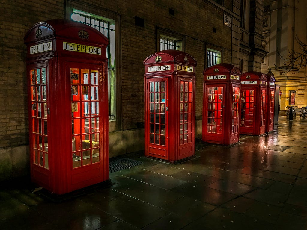 a row of red British telephone booths (call boxes) along a street
