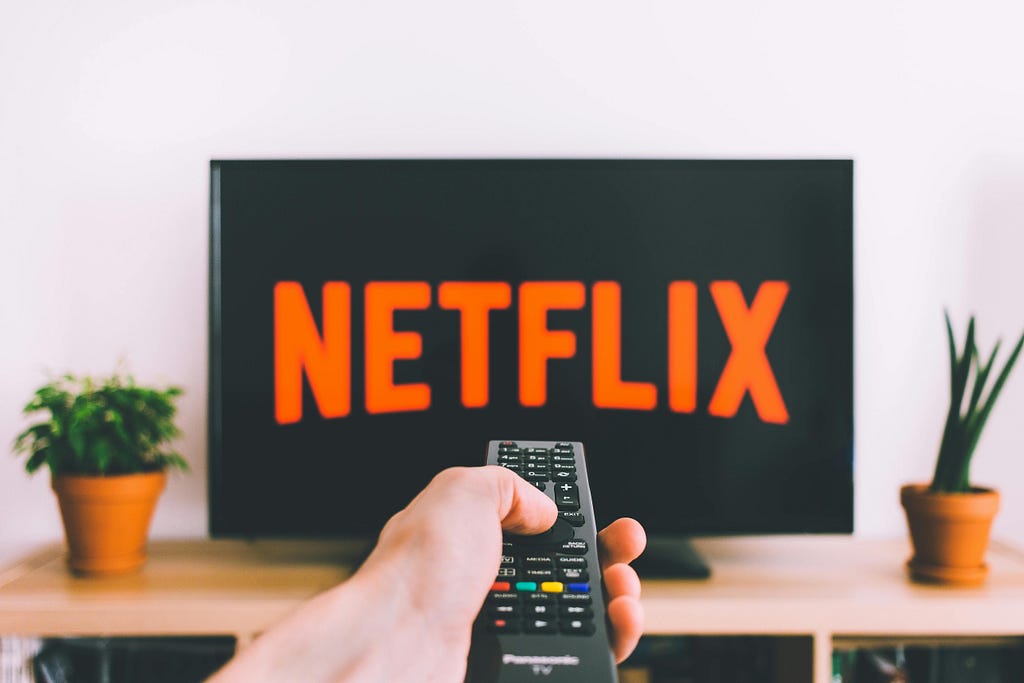 A hand pointing a TV remote at a television screen with the Netflix logo on it