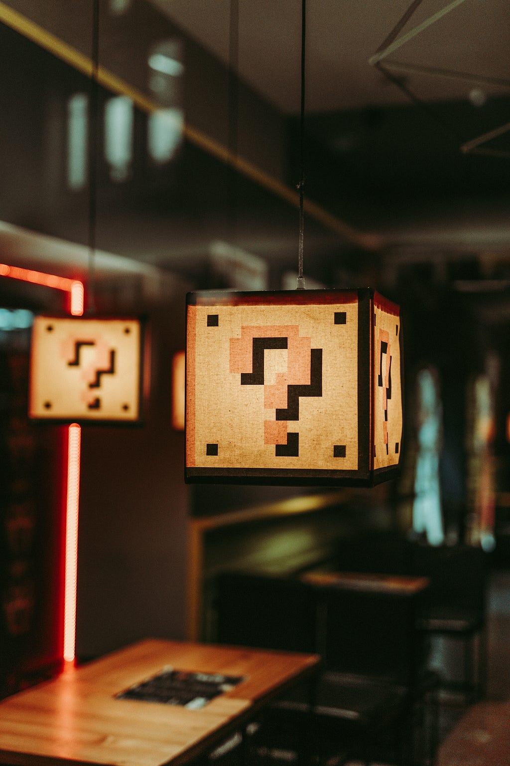 A wooden table topped with illuminated light fixtures. The fixtures are overlayed with question marks in the style of Super Mario Brothers.