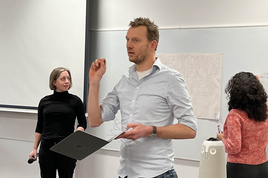 Professor Anne Forster and Dr Sarah Astill present their ideas to the collaborative lab. Prof Chatterton is talking to the audience, holding a laptop, and Dr Radhika is drawing on the whiteboard behind.