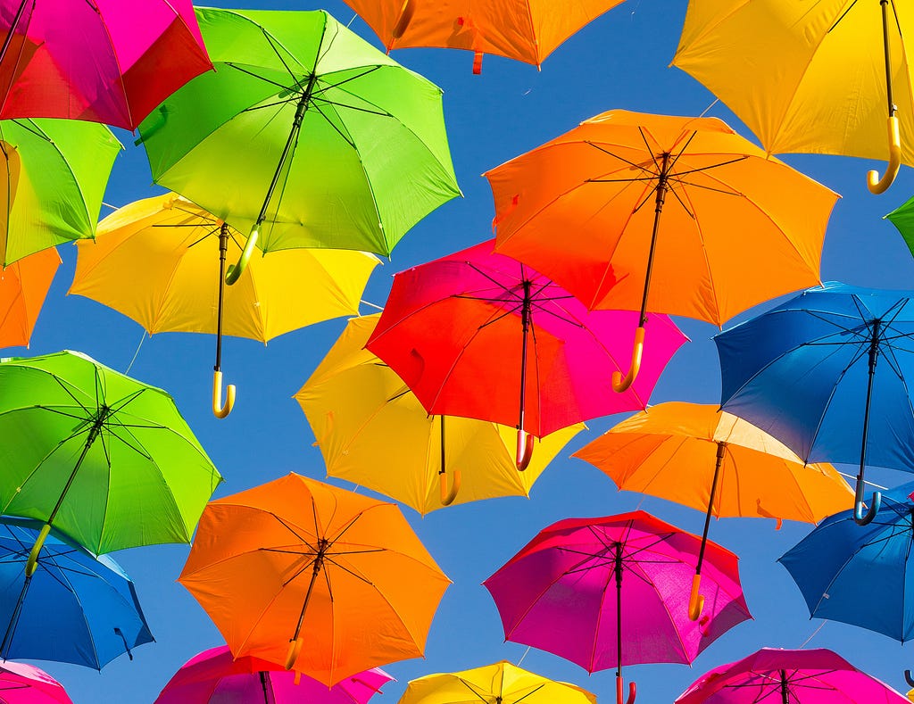 Colorful umbrellas in rainbow colors floating down in blue sky.