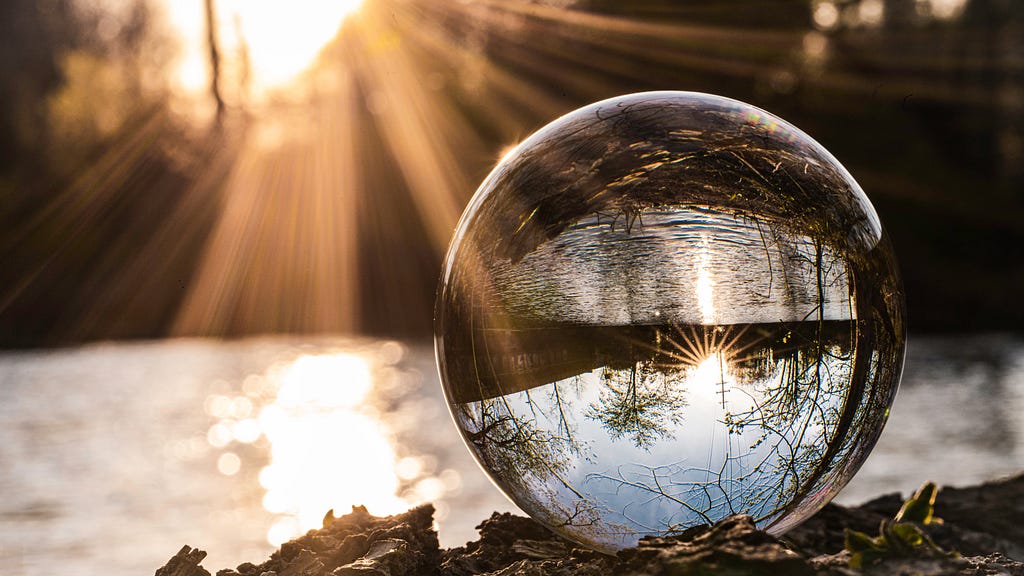 Photo of glass ball, reflecting nature scene upside down, with sun streaming in from top left with golden glow on everything.