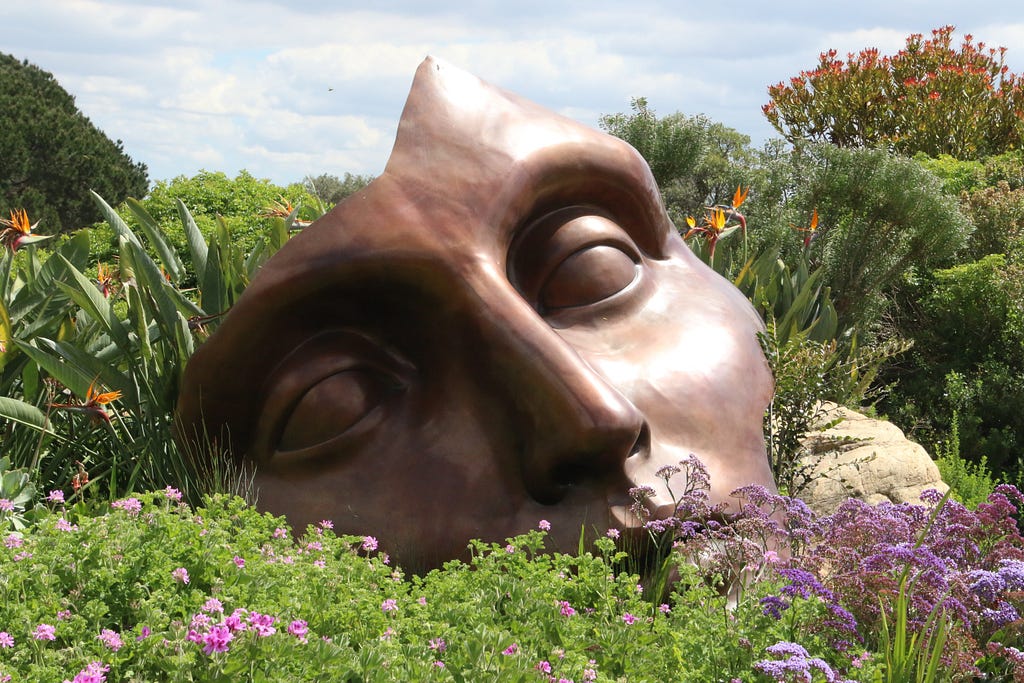 Statue of a figure’s face in a meadow of flowers.