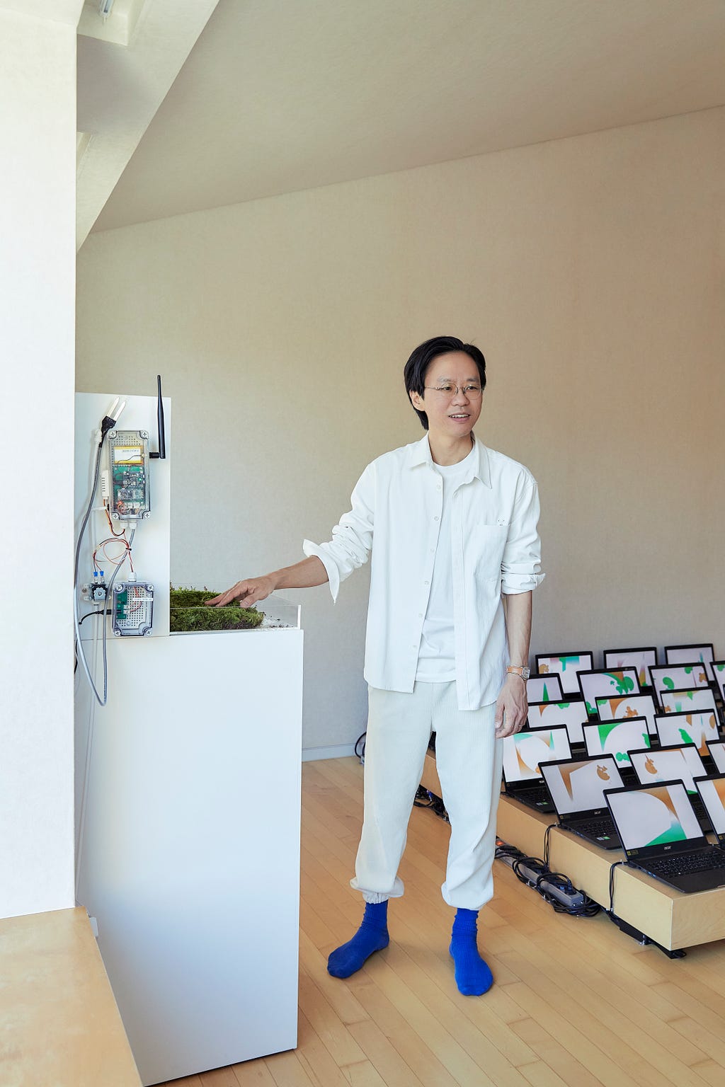 Taeyoon wearing white, in a room with many laptops that is displaying virtual garden