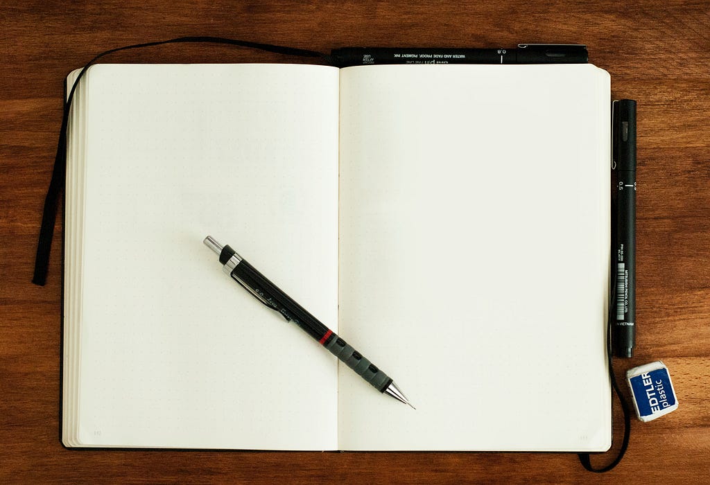 Open notebook on a wooden table opened to blank pages. Pen placed in the middle of the notebook.