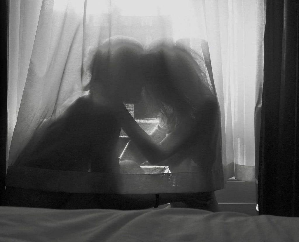 a couple holding each other in intimate embrace behind a sheer curtain