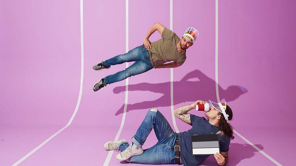 On a pink backdrop, a prone photographer’s assistant holds an exposure chart. Another man is frozen in a jump, mid-air