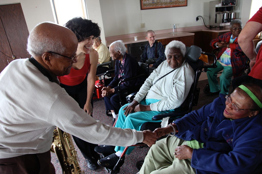 Irv Williams and Maria Genne (left) shaking hand and greeting seated participants (right) at a Kairos Alive event.