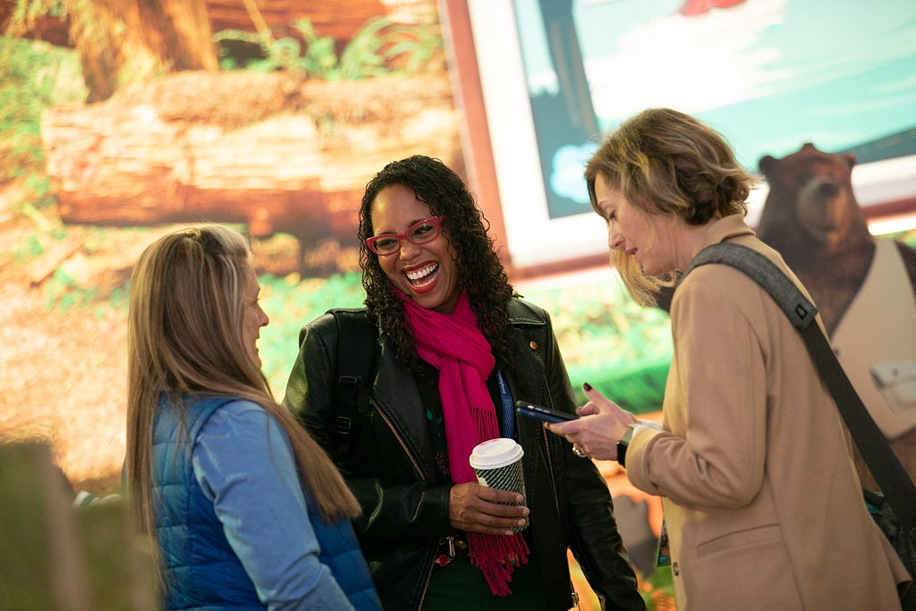 Three women stand together talking and laughing at a recent Salesforce event.