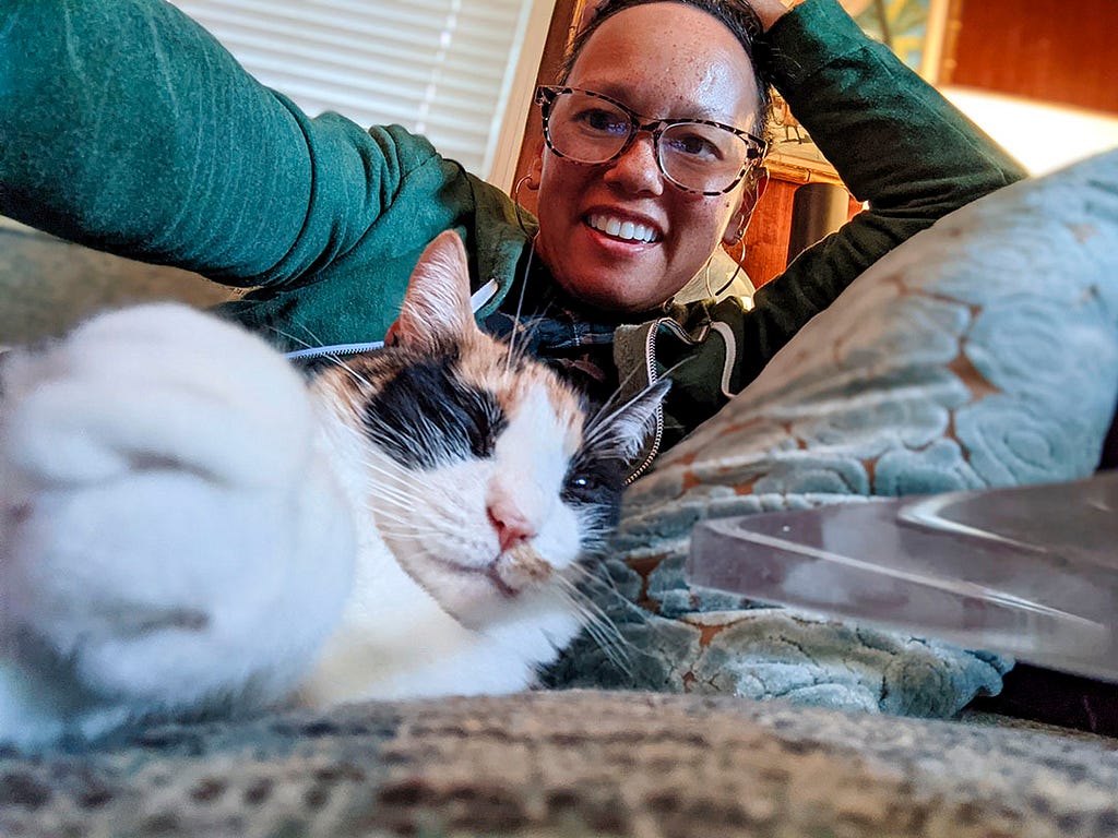 A lady laying snuggling on a couch with a cat