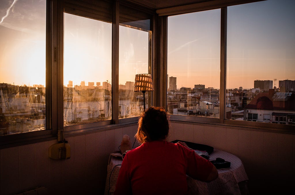 The back of a woman writing on a table with the sunrise over the city of Barcelona in the background.