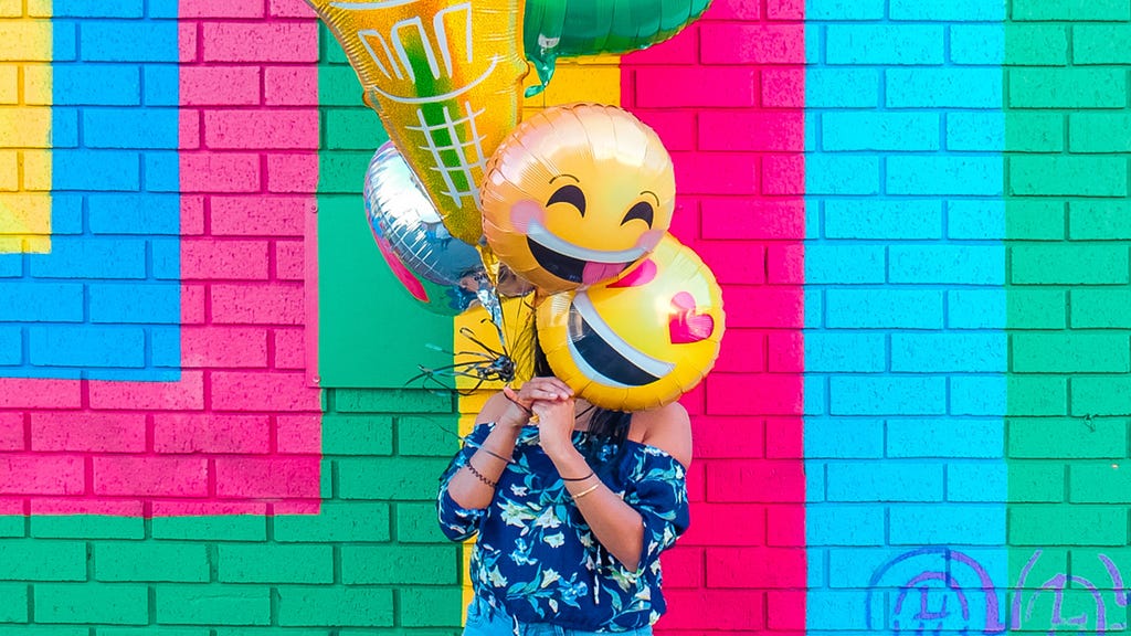 A young women holding balloons in the shape of emojis (laughing and heart eyes)