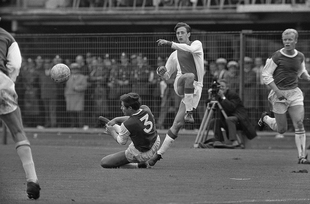 Johan Cruyff kicking the ball while an opponent slides in for a tackle