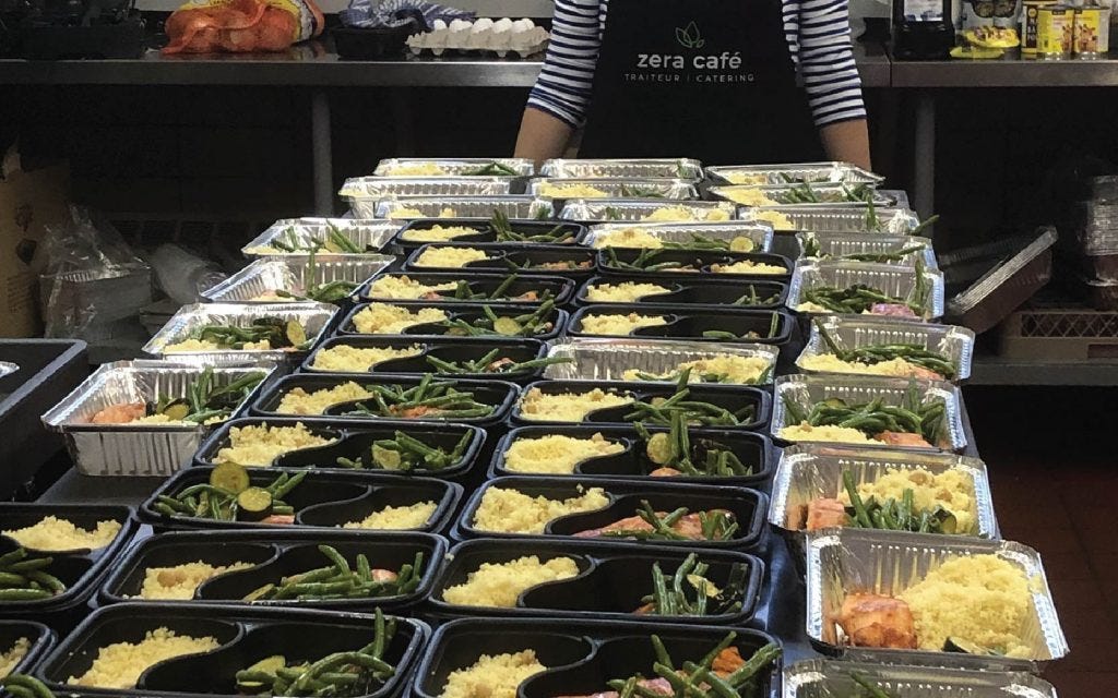 A bunch of meal prep trays with food are laid out in the catering kitchen of Zera Café.