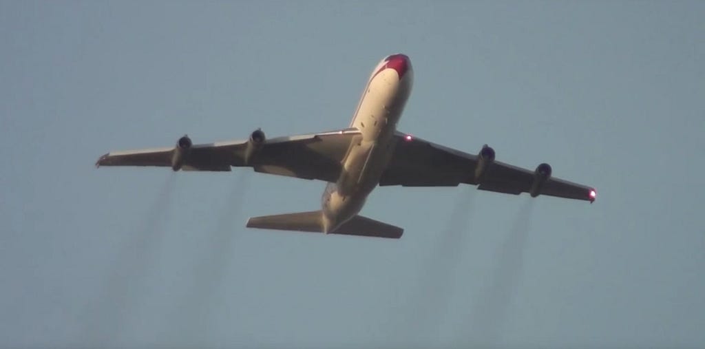 An aeroplane in the air. You can see black pollutants out of its engines.