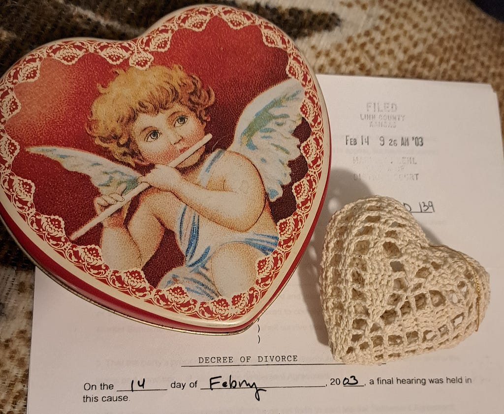 A decorative red heart with a sad, winged Cupid playing a flute and a white crocheted heat ornament have been laid across the top of the first page of a divorce decree, dated February 14, 2003. Photo by Linda Bittle