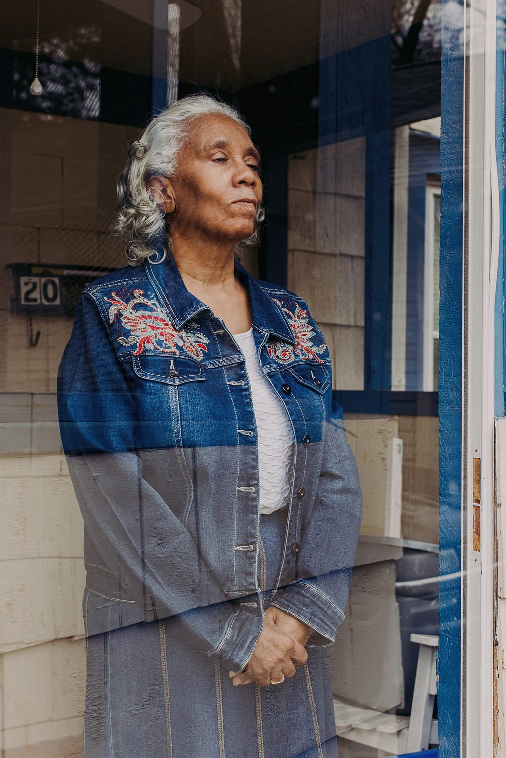 Portrait of Camille Givens, 69, looking through a glass door at her home in Kansas City.