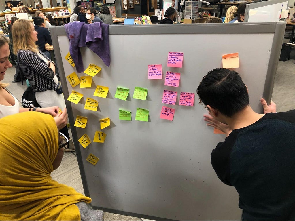 Members of our team writing out ideas we want to incorporate into our prototype onto sticky notes and putting them on a white board.