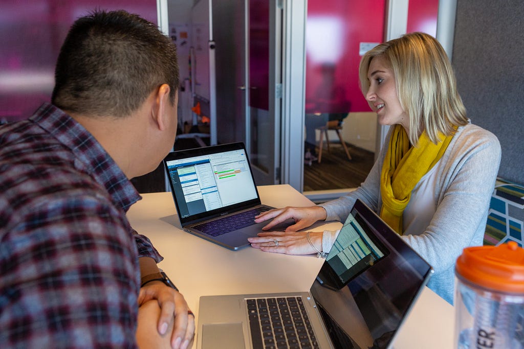 Two employees collaborate on a project on their laptops at a desk