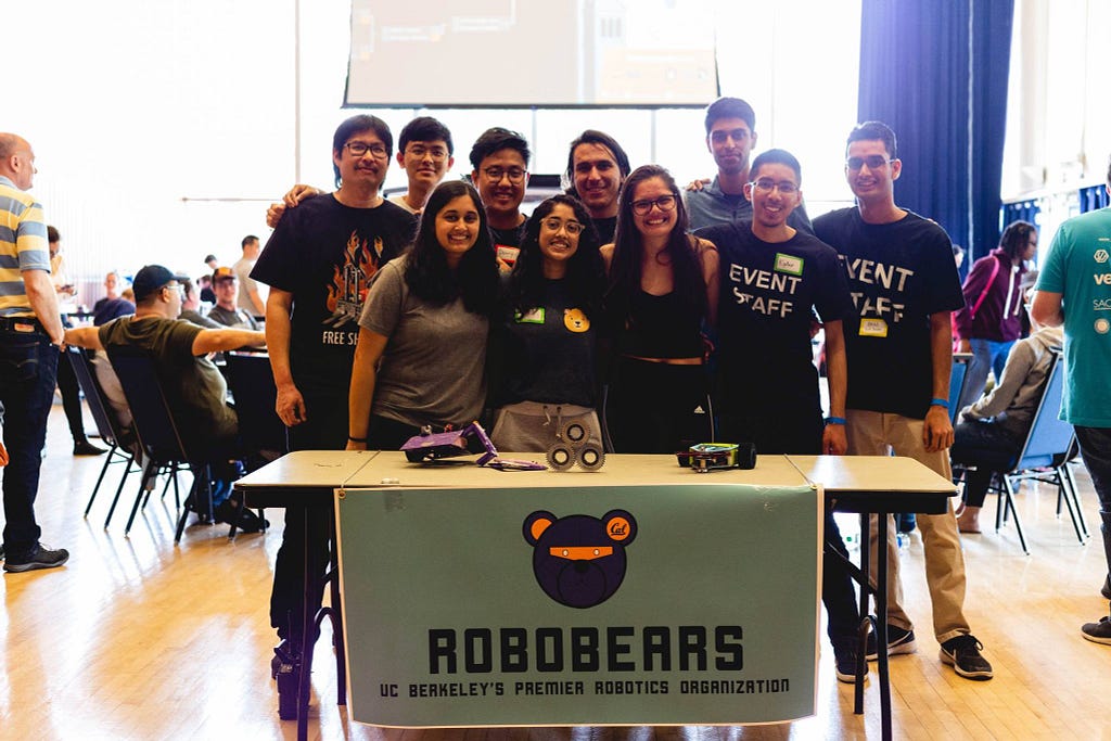 Group of students poses for a photo behind a table with a banner that says “RoboBears.”