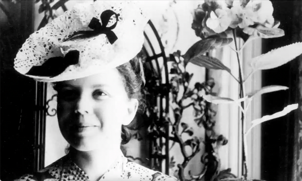 Portrait of Jeannie Rousseau, wearing a hat adorned with ribbons
