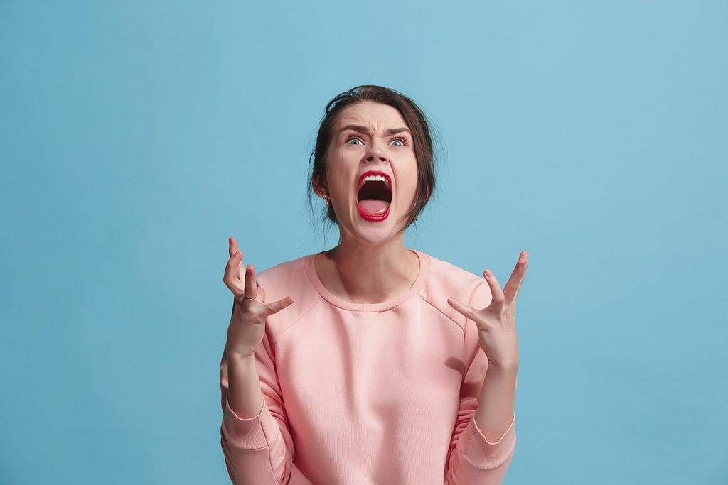 Picture of brunette woman in pink shirt screaming against a blue background