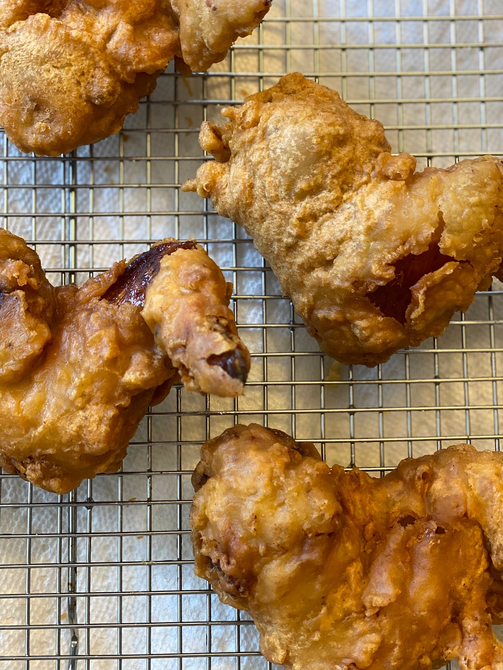 Crispy golden fried chicken wings sit on a cooling rack.