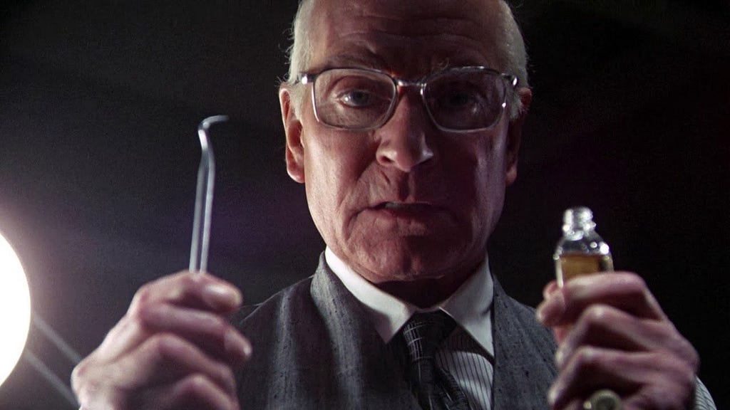 A menacing still frame from the movie Marathon Man of Sir Laurence Olivier holding up a tooth scraper in one hand and a small bottle in the other