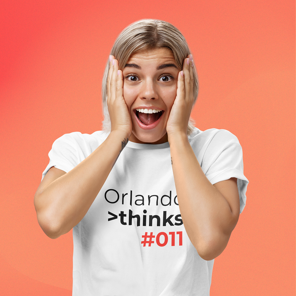 A woman holding her cheeks. She seems very surprised. She wears a shirt with the title logo “Orlando thinks #011” printed on it.