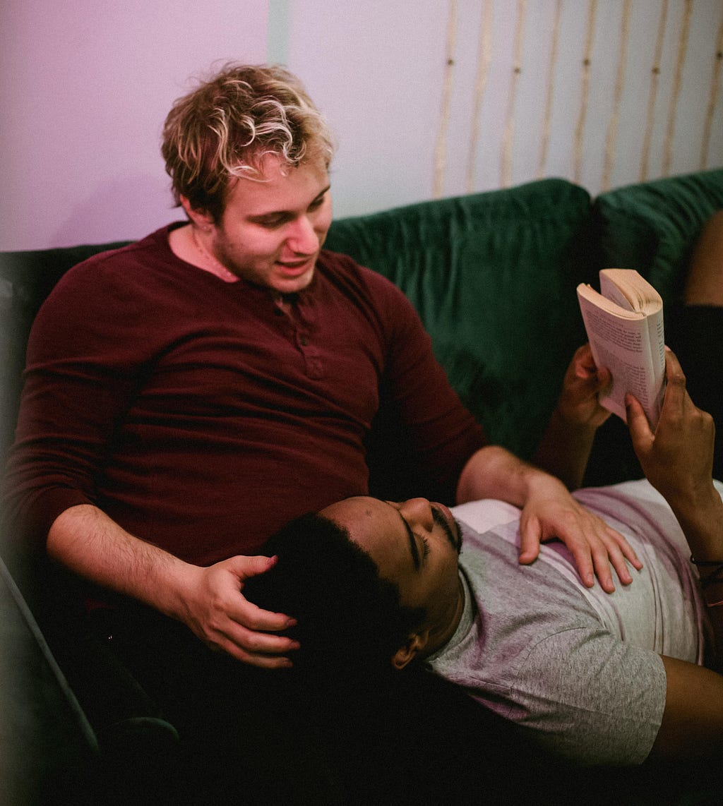 A man reading and resting his head on another man’s lap.