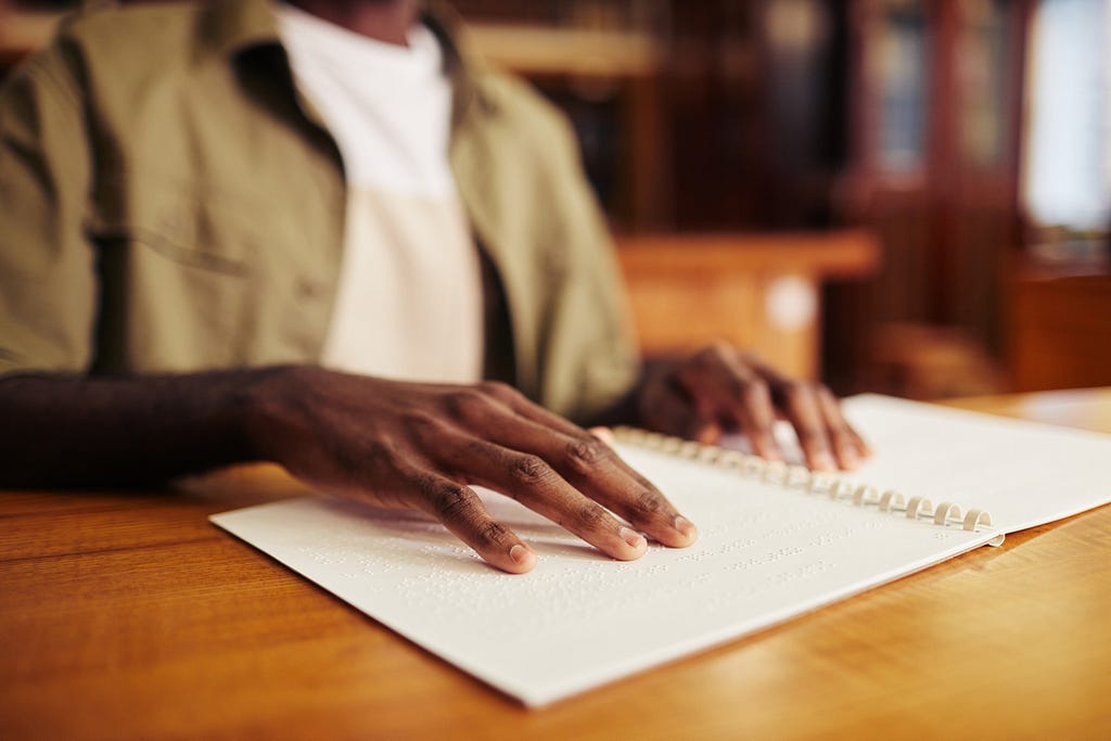 A man in a green jacket with hands on a white book with braille on it.