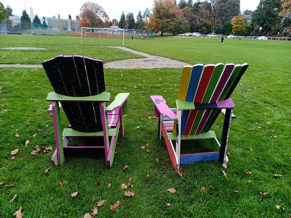 Two adirondack chairs overlooking a public park.