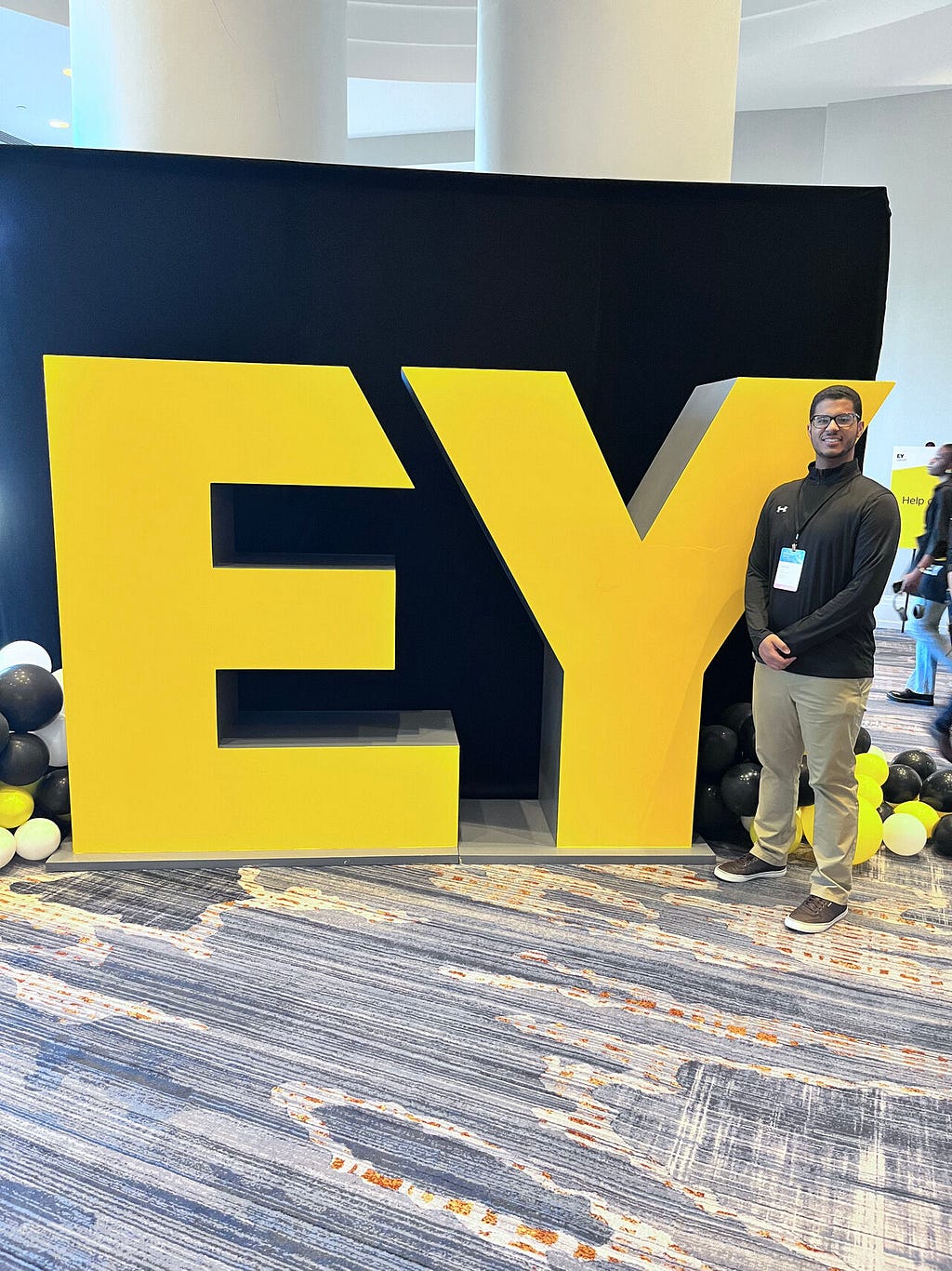 Tomas standing in front of a large “EY” sign at National Launch Training in Baltimore, MD.