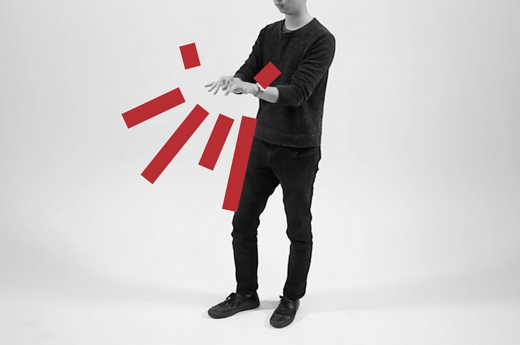 The image shows a person in a black outfit standing in a minimalist, white background. The person is gesturing with their hands, and red graphic elements are superimposed over the image, radiating outwards from their hand in stylized shapes. This suggests the use of gesture-based interaction or visualization, possibly related to augmented reality or gesture control technology.